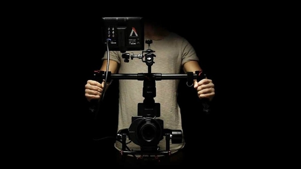 Kameramann mit Gimbal-Kamera im schwarzen Raum, Kamera und Gimbal durch Spotlicht im Fokus.